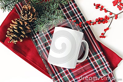 Winter still life. Blank coffee mug, fir tree branch, holly berries and pine cones. Checkered tartan plaid. Christmas Stock Photo