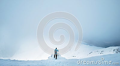 Winter Trekker staying on mountain peak he climbed and enjojing wide panorame view of valley covered by storm clouds. Active Stock Photo