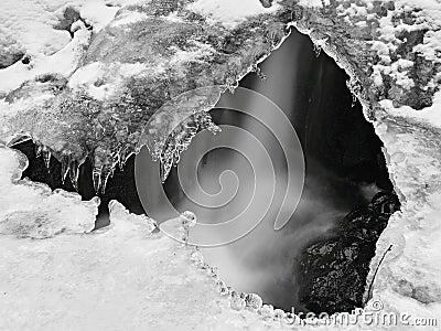 Winter view through ice hole to thin water stream on cascades below. Stock Photo