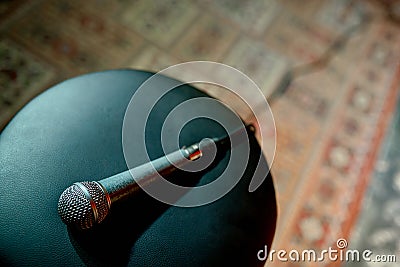 A wired scuffed microphone lies on a chair stool on stage with a vintage carpet in front of the stand. Stock Photo