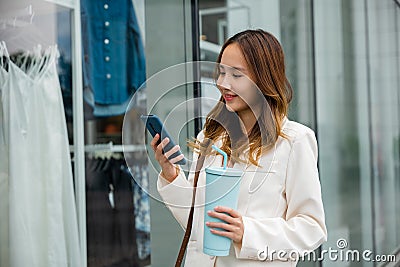 Marketing on the go ,young woman holding a tumbler mug and smartphone while walking Stock Photo