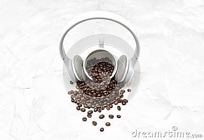 Wireless overhead headphones on a coffee cup and roasted coffee beans scattered on a textured concrete table Stock Photo