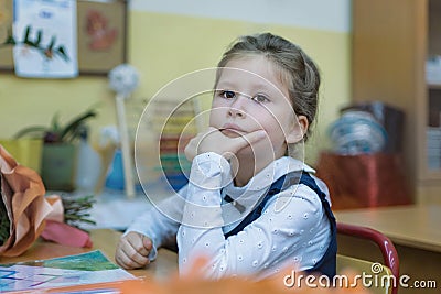 A wise schoolgirl of primary classes sits at a desk and listens to a lesson. Day of knowledge Stock Photo