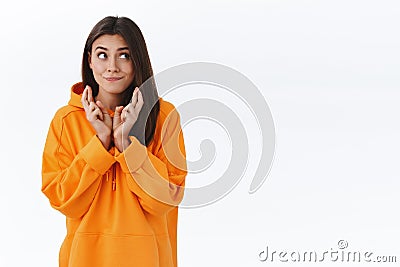 Wishful dreamy gorgeous brunette girl in orange hoodie, smiling and looking aside while maing wish, cross fingers good Stock Photo