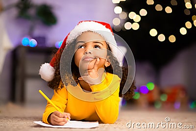 Wistful little afro girl thinking about letter to Santa Claus Stock Photo