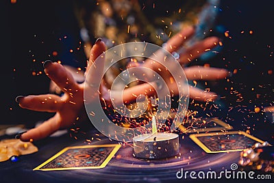 A witch`s hands light the flame of a candle standing near two tarot cards. Close-up. Sorcery and astrology Stock Photo