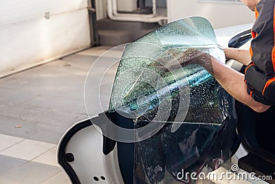The wizard for installing additional equipment sticks a tint film on the side front glass of the car and flattens it by hand to Stock Photo
