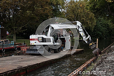 White Cat industrial digger floating on a raft barge on a river canal and excavating the bank Editorial Stock Photo