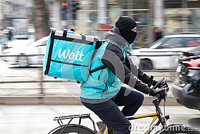 Wolt courier with a delivery bag riding bike in busy city street full of pedestrians, profile view Editorial Stock Photo