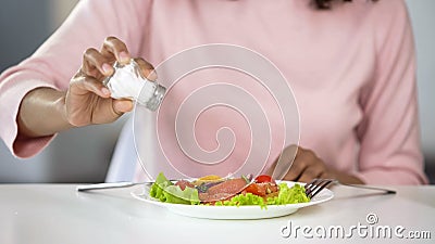 Woman adding too much salt to her food, unhealthy eating, dehydration problems Stock Photo