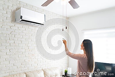 Woman Adjusting Temperature Of Air Conditioner With Remote Stock Photo