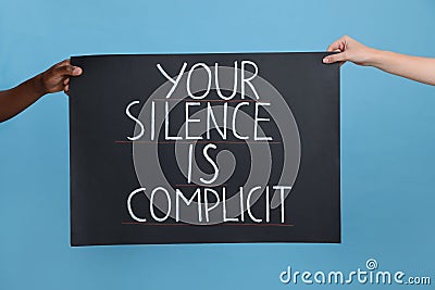 Woman and African American man holding sign with phrase Your Silence Is Complicit on light blue background, closeup. Racism Stock Photo