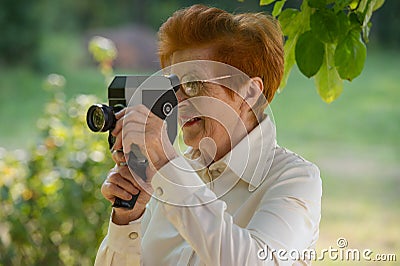 Woman ages shoots a movie camera park. Stock Photo