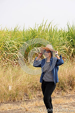 Woman agriculturist standing with two hands on her hat and wearing Long-sleeve denim shirt on the sugarcane farm Stock Photo