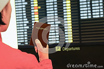 Woman in airport holding passport ,looking at flight information board Stock Photo