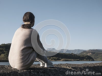 Woman alone sitting on stone coast and looking at sea and mountan Stock Photo