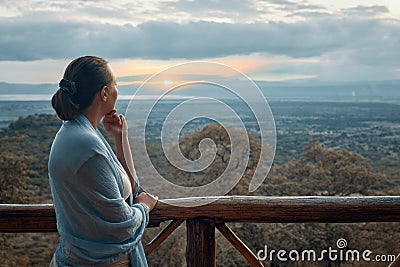 Woman alone on terrace watching sunset over mountains during summer vacation Stock Photo