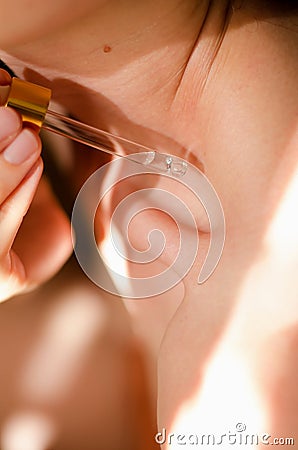 A woman applies oil to body. A drop of essential oil drips from a pipette onto a woman`s collarbone. Serum for the body Stock Photo
