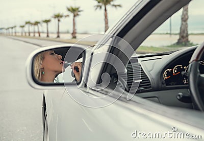 Woman apply lipstick looking in rear view car mirror Stock Photo