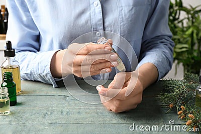 Woman applying essential oil on wrist at wooden table, Stock Photo