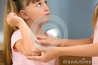 Woman applying plaster on girl`s elbow indoors Stock Photo