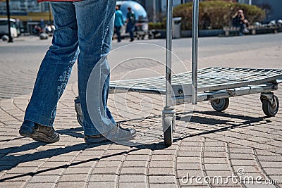 Woman approaches and takes a trolley to transport things. City street Stock Photo