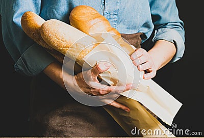 A woman in an apron holds various fresh bread loaves with golden crisp in her hands. Homemade alternative bread Stock Photo