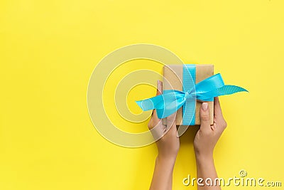 Woman arms holding gift box with blue ribbon on color background, top view Stock Photo