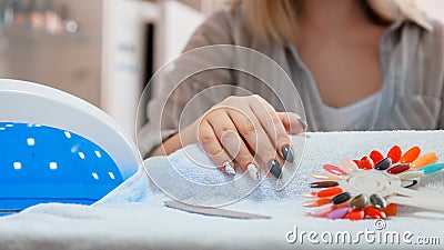 Woman with artificial acrylic nails picks up new polish color during manicure procedure. Manicure process in beauty Stock Photo