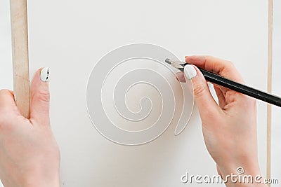 Woman artist`s hand with a large simple pencil, draws on a clean white canvas, close-up. Stock Photo