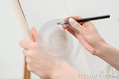 Woman artist`s hand with a large simple pencil, draws on a clean white canvas, close-up. Stock Photo