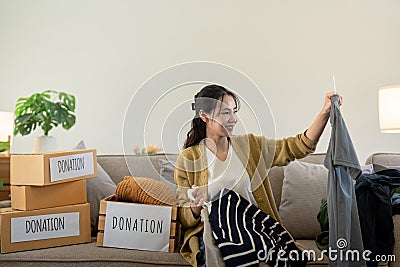 Woman asian holding donation box full with clothes and select clothes. Concept of donation and clothes recycling Stock Photo