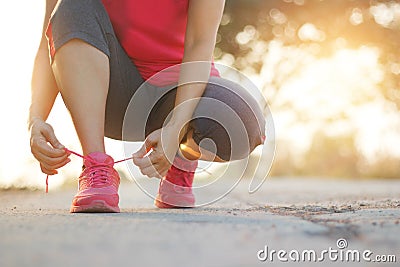 Female athlete tying running shoes on rural street in sunset back Stock Photo