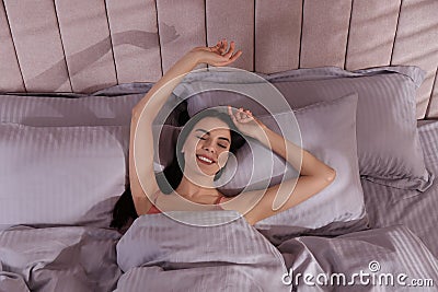 Woman awakening in comfortable bed with light grey striped linens, above view Stock Photo