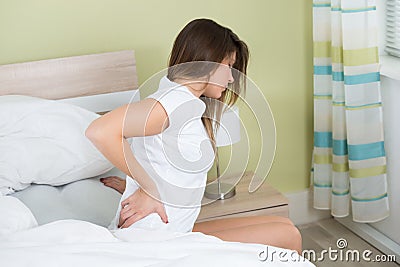 Woman With Back Pain Sitting On Bed Stock Photo