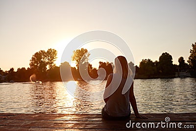 Woman from back sitting and looking sunset Stock Photo