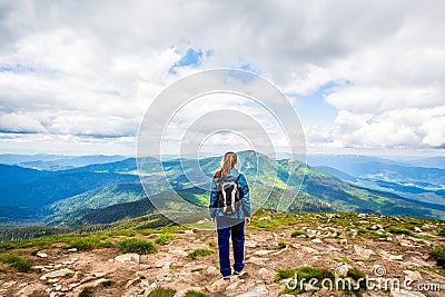 Woman with backpack rise to the mountain top. Girl stands atop a rock just off a hiking trail mountain range back Stock Photo