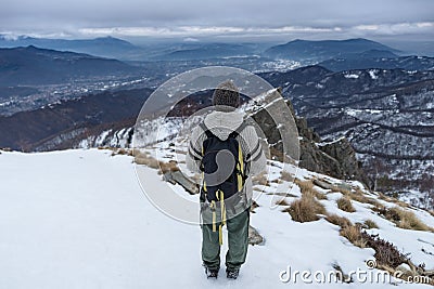 Woman backpacker hiker looking at view high up on the Alps. Rear view, winter cold snow, dark clouds and overcast. Editorial Stock Photo