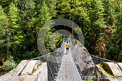 Woman backpacker on trekking path crossing a suspended bridge in Annapurna Conservation Area, Nepal Editorial Stock Photo