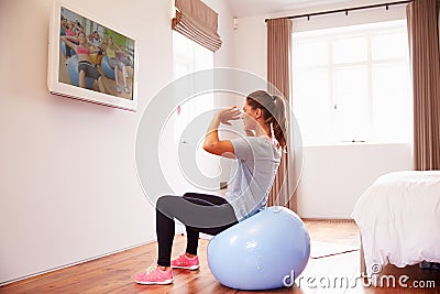 Woman On Ball Working Out To Fitness DVD On TV In Bedroom Stock Photo