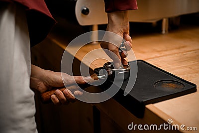 woman barista presses ground coffee using tamper. Close-up view on hands with portafilter Stock Photo