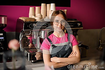 woman barista stands with her arms crossed on her chest and professional coffee machine in the background Stock Photo