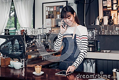 woman barista take order by mobile and tablet,asia female waitress using digital device in coffee shop business at counter bar in Stock Photo