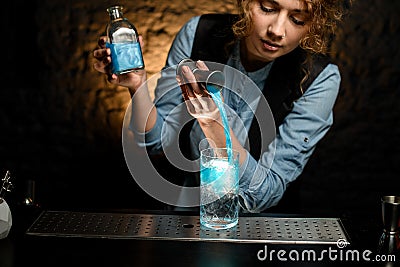 Woman bartender gently pours drink from jigger into glass of cold water Stock Photo