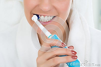 Woman In Bathrobe Brushing Teeth With Electric Toothbrush Stock Photo