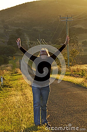 Woman in beautiful countryside raising arms to thank God for answered prayer Stock Photo
