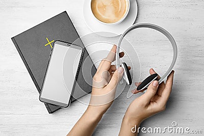 Woman with Bible, phone, cup of coffee and headphones at white wooden table. Religious audiobook Stock Photo