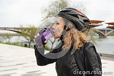 A woman in a bicycle helmet drinks water after cycling. Sportswoman drinks water from a bottle Stock Photo