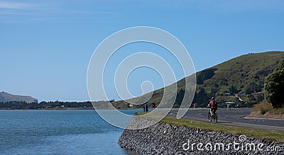 A woman biker cycling along water in Otago Peninsula near Dunedin in the South Island in New Zealand Stock Photo