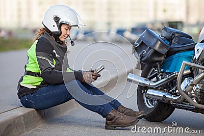 Woman biker trying to find road with sat nav while sitting on roadside near motorcycle Stock Photo